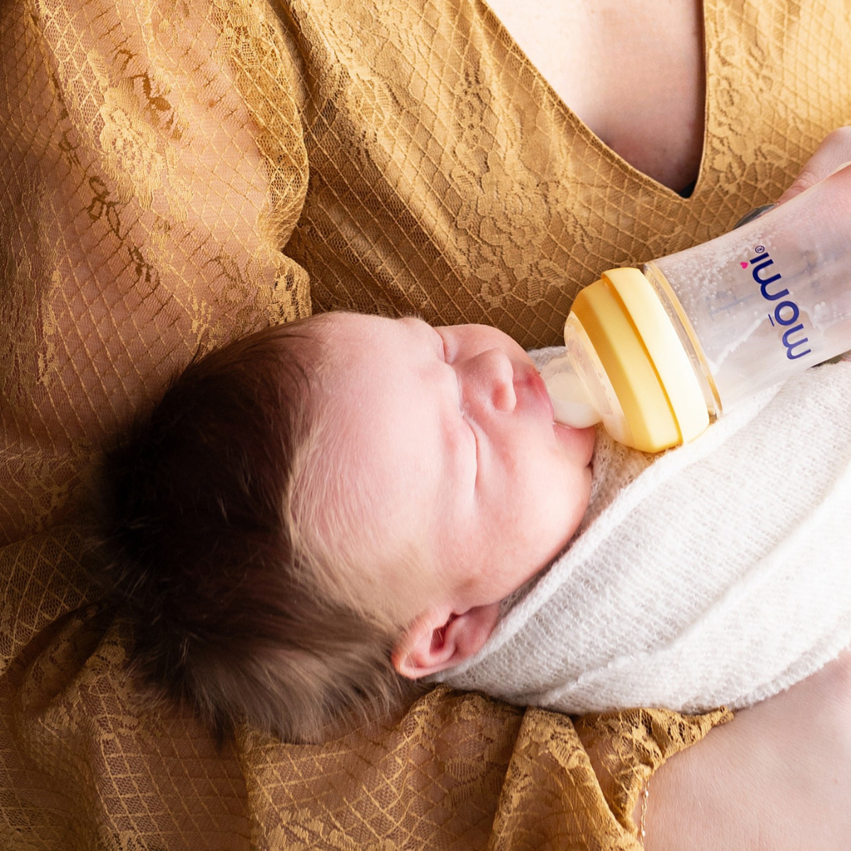 Newborn baby being fed from a mōmi  bottle with a sundrop yellow collar in mother's arms